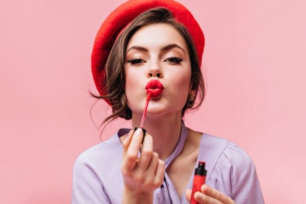 portrait young girl red beret painting her lips with bright lipstick pink background e1638956201557